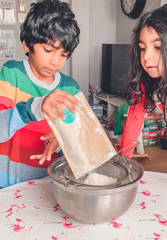Children pouring biscuit mix into sieve